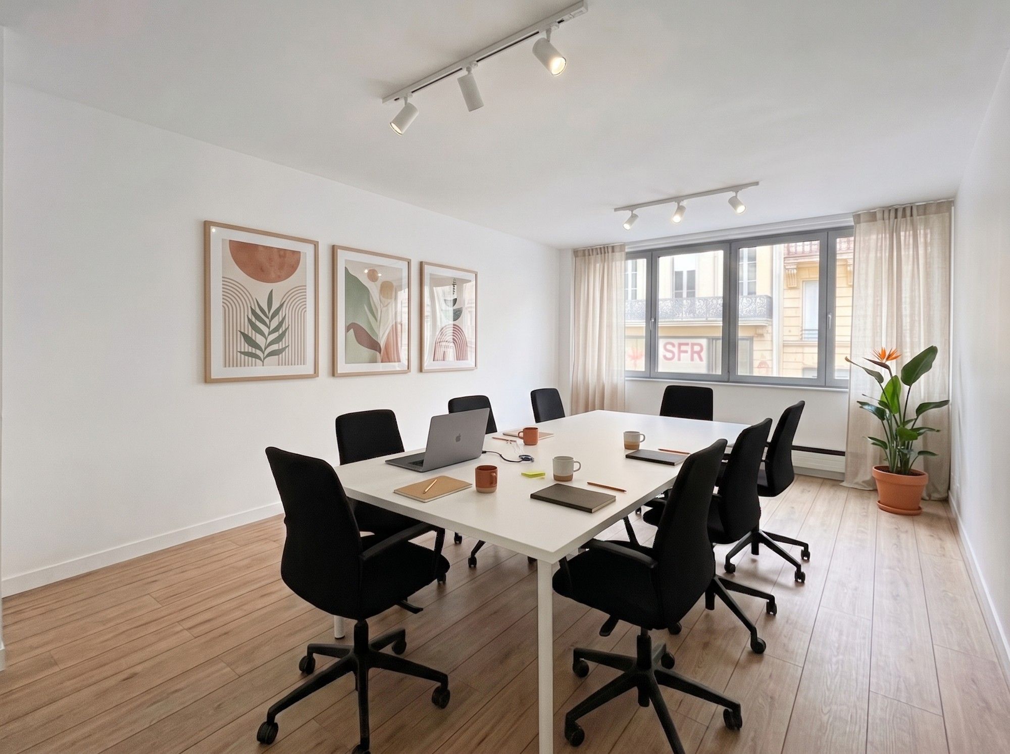 Pièce fermée avec une grande table blanche et huit fauteuils, utilisable en bureau ou en salle de réunion