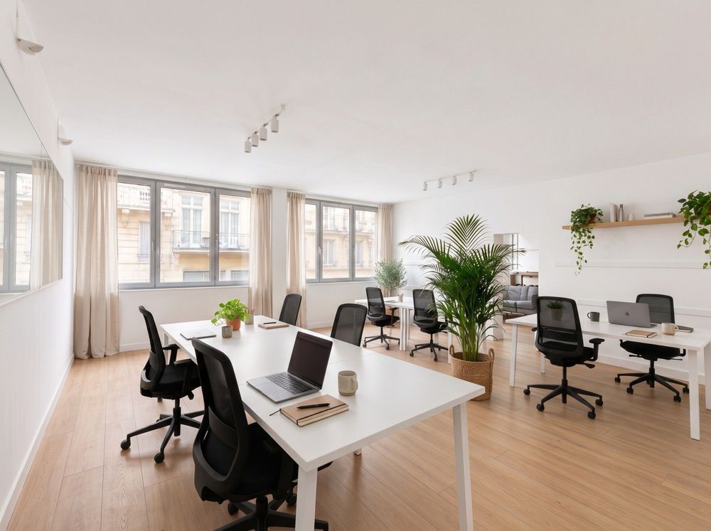 Bureau lumineux avec postes de travail blancs, fauteuils noirs et plantes, fenêtres sur la rue