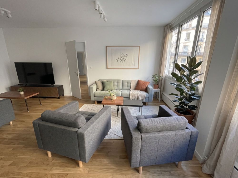 Espace détente avec deux fauteuils, un canapé et une grande plante près des fenêtres